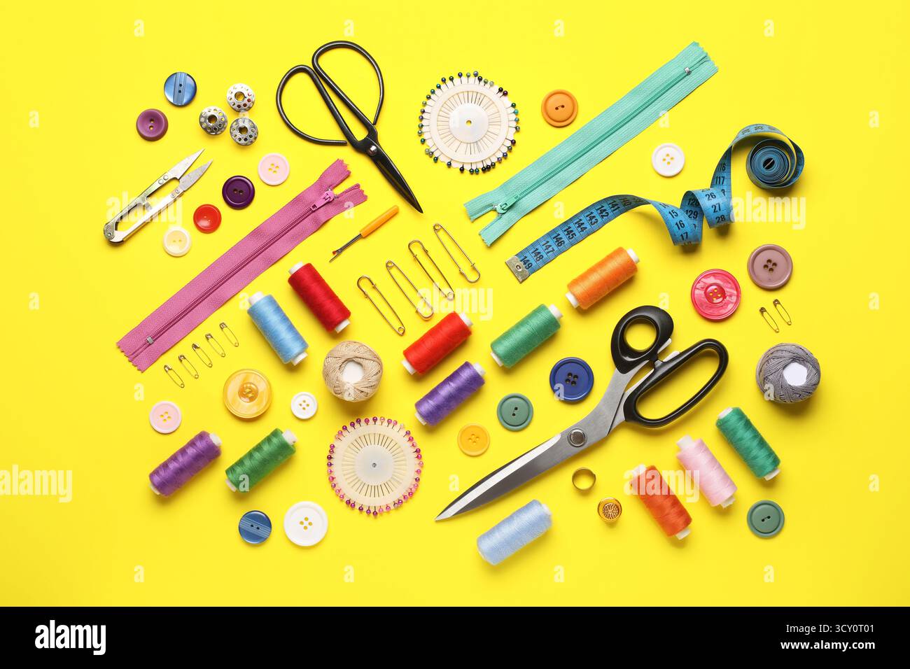 Composition with different thread spools and sewing accessories on yellow background Stock Photo