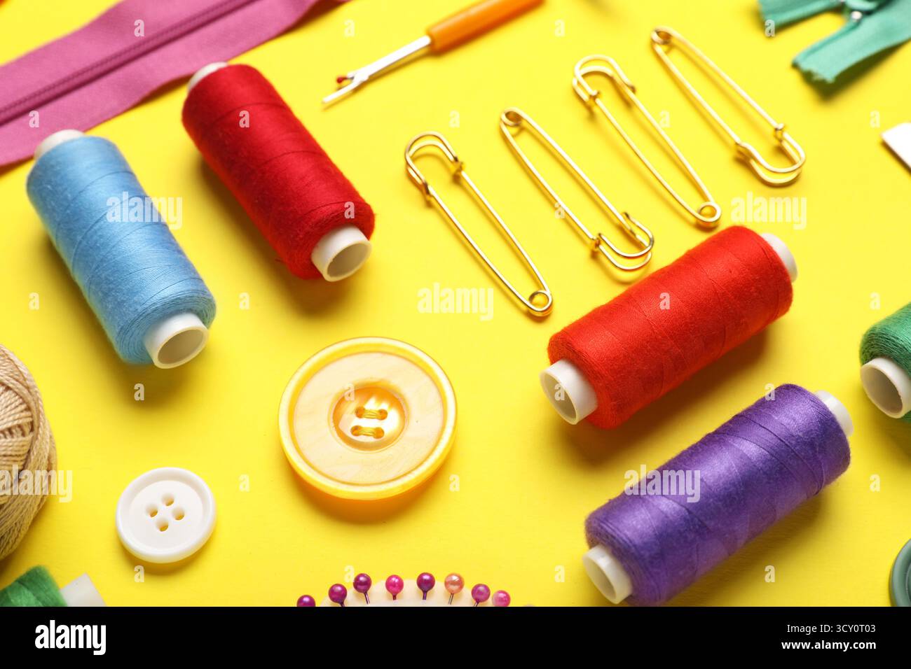 Composition with different thread spools, buttons and pins on yellow background, closeup Stock Photo