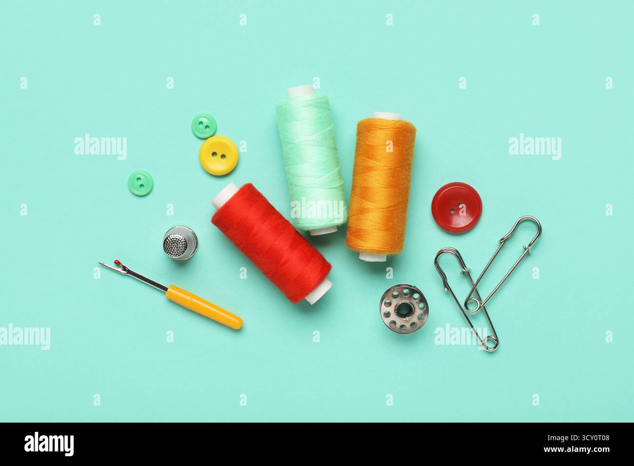 Composition with thread spools, thimble and buttons on mint background Stock Photo