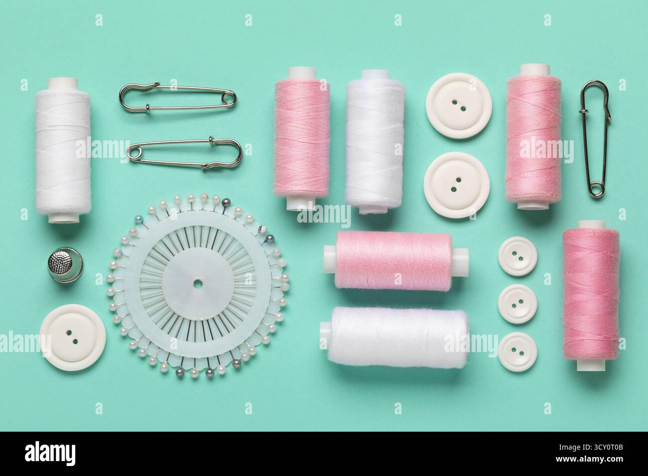 Composition with thread spools, ball pins and buttons on mint background, closeup Stock Photo