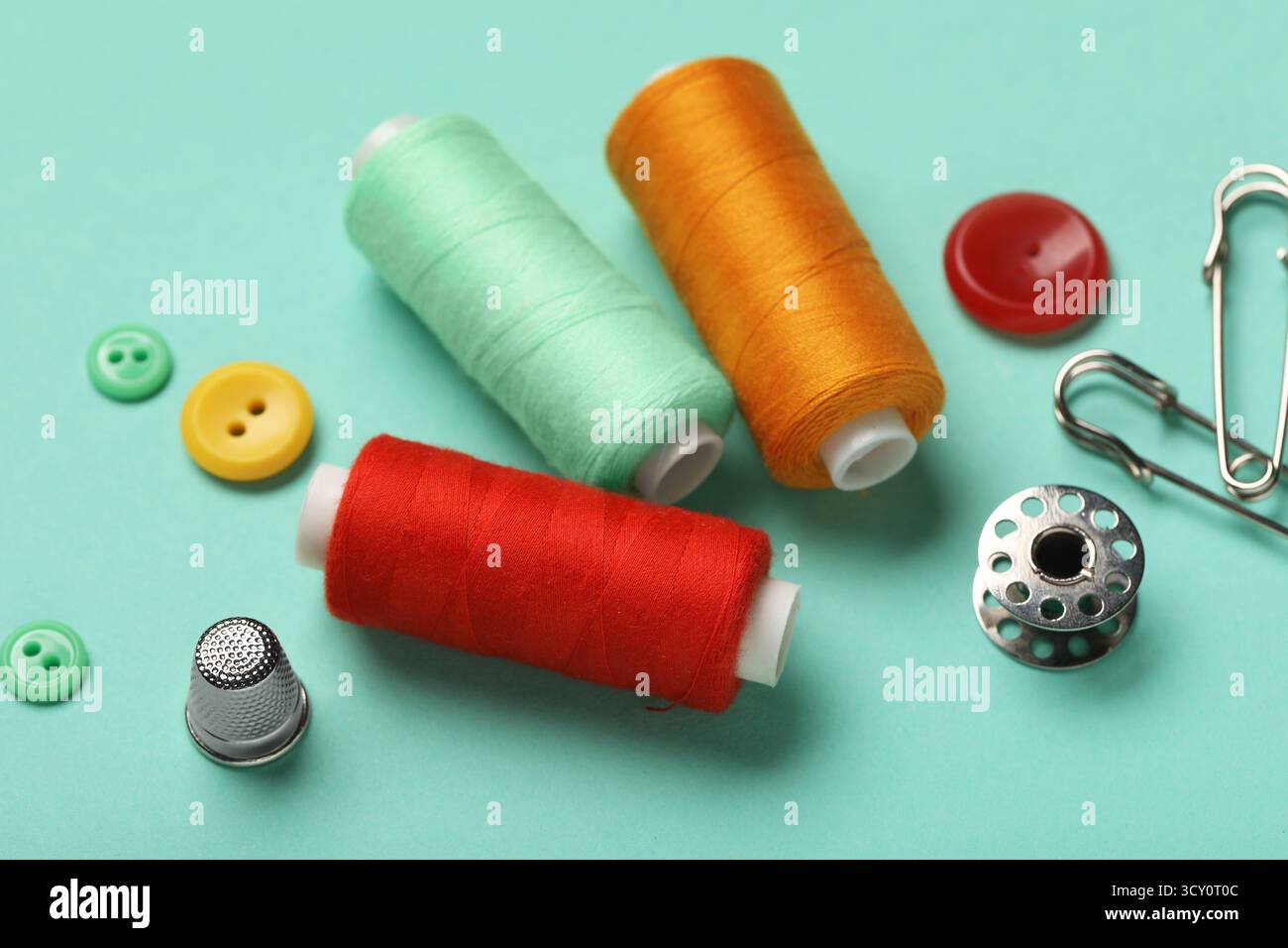 Composition with thread spools, thimble and buttons on mint background, closeup Stock Photo