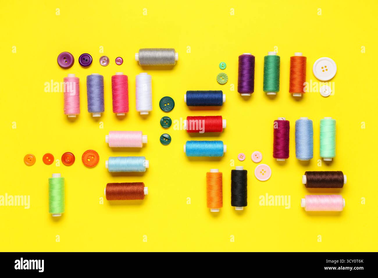 Composition with many different thread spools and buttons on yellow background Stock Photo