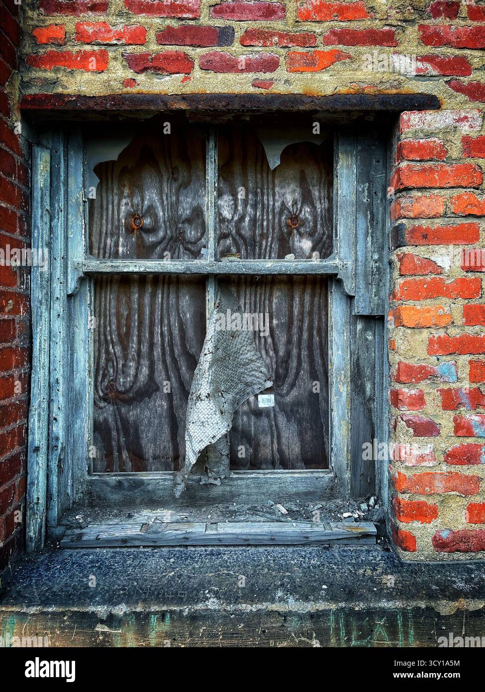 Old brick wall with a weathered wooden window, featuring chipped paint and a torn screen panel, displaying urban decay - Smartphone Captured Stock Image
