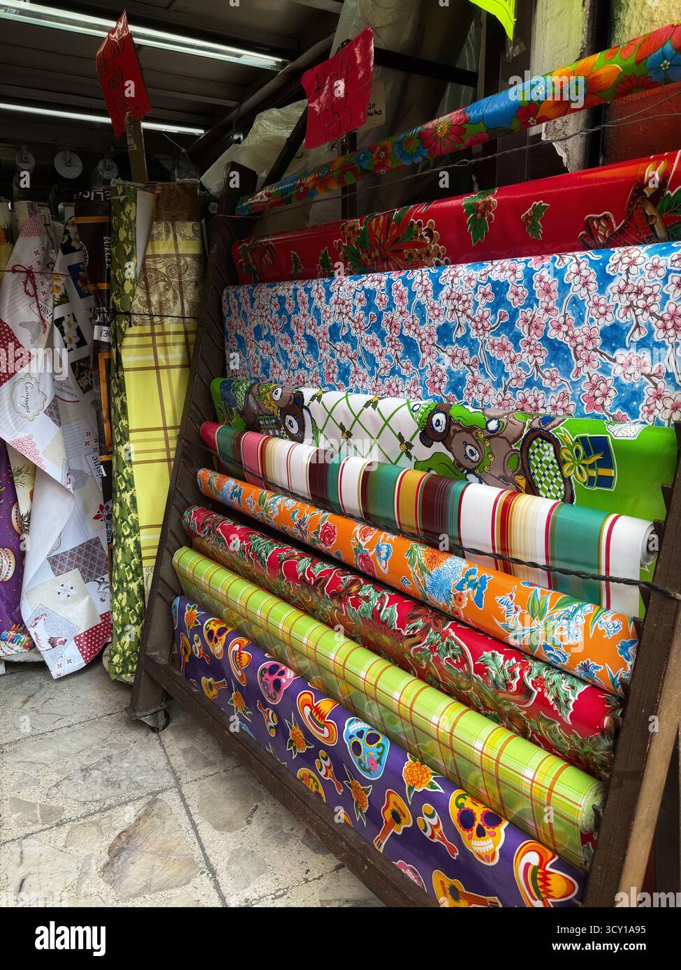 Colorful rolls of vibrant patterned fabric displayed in a market stall with various designs and textures in a street market setting - Smartphone Captured Stock Image