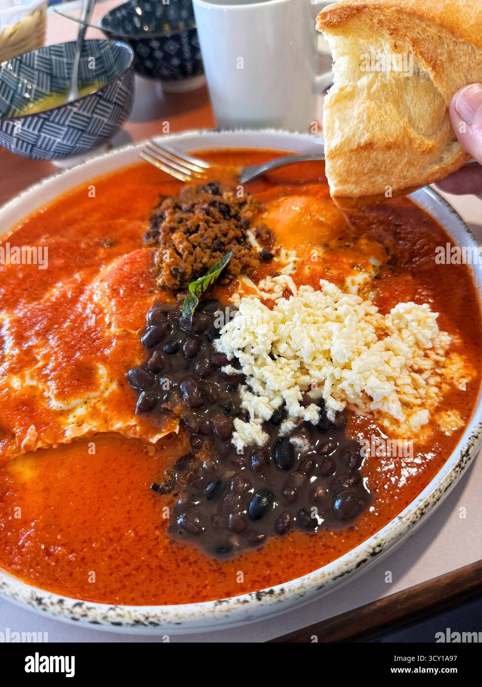 A delicious Mexican breakfast dish with red sauce, black beans, cheese, and bread on the side - Smartphone Captured Stock Image