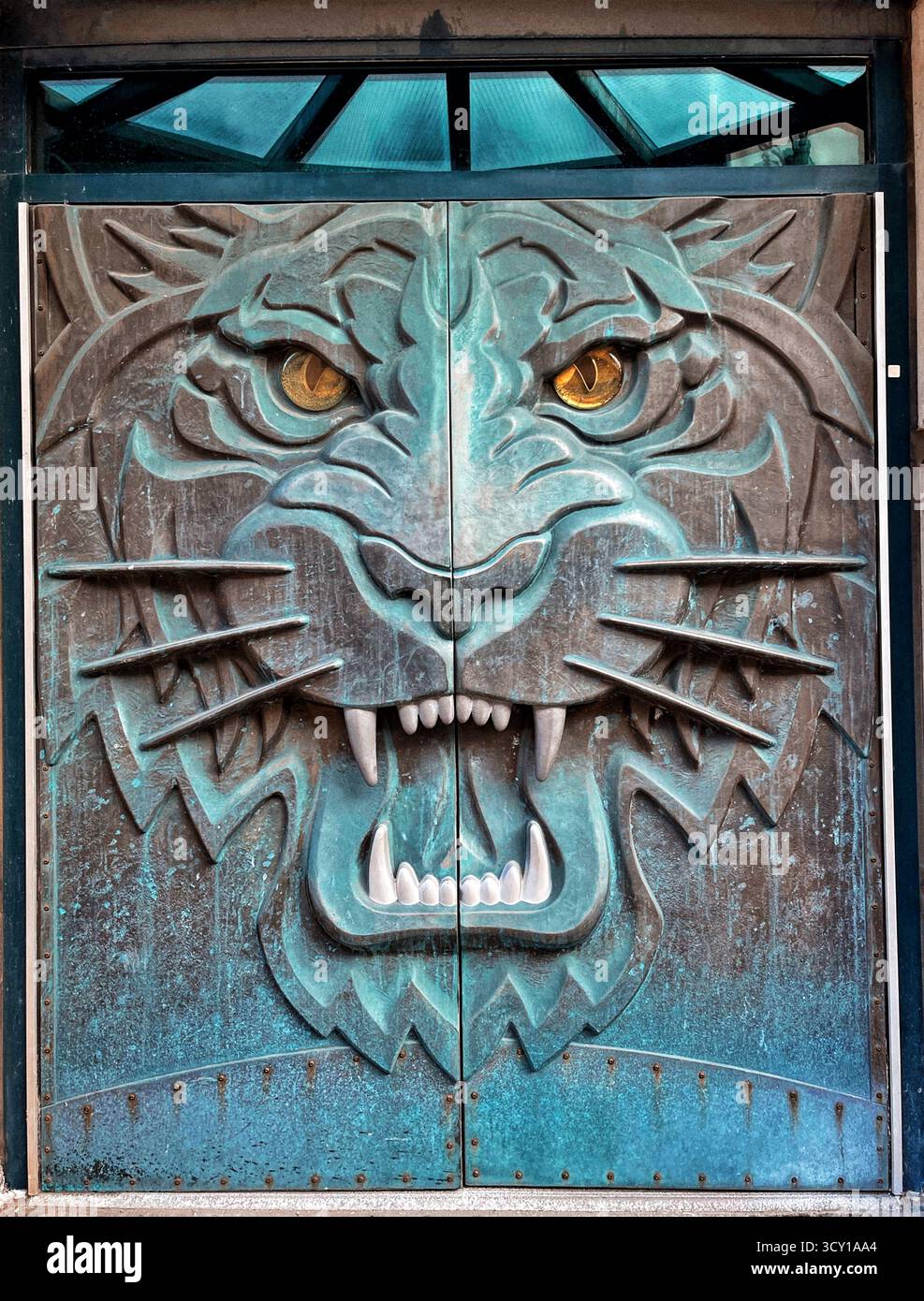 Intricately designed metal door featuring a fierce lion face with striking yellow eyes and sharp details, symbolizing strength and protection - Smartphone Captured Stock Image