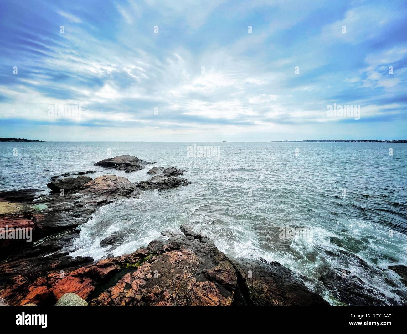 Rocky coastline under a cloudy sky with waves crashing along the shore, creating a serene and dramatic seascape - Smartphone Captured Stock Image