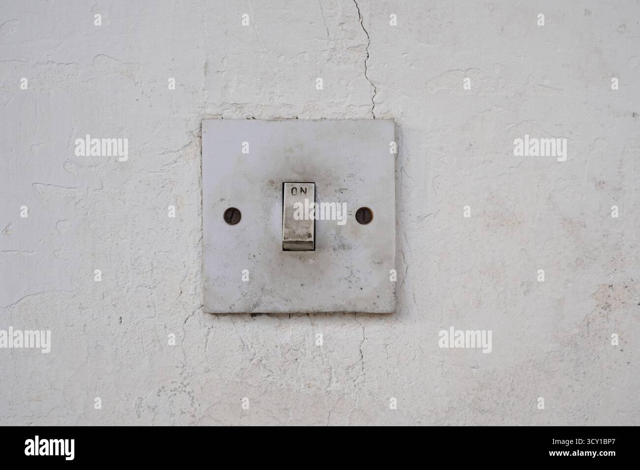 An old, dirty light switch on a cracked white wall Stock Photo
