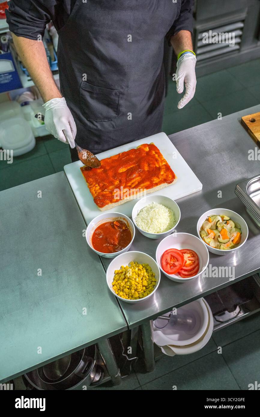 Anonymous male chef with black apron spreading tomato sauce over ...