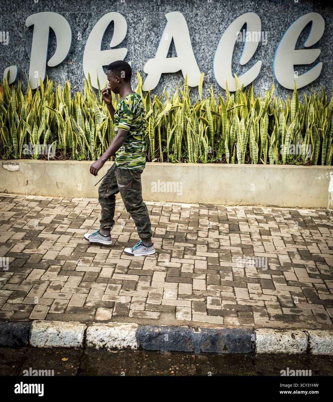 RWA RWANDA RUANDA Kigali A man in camouflage fashion passes a Peace ...