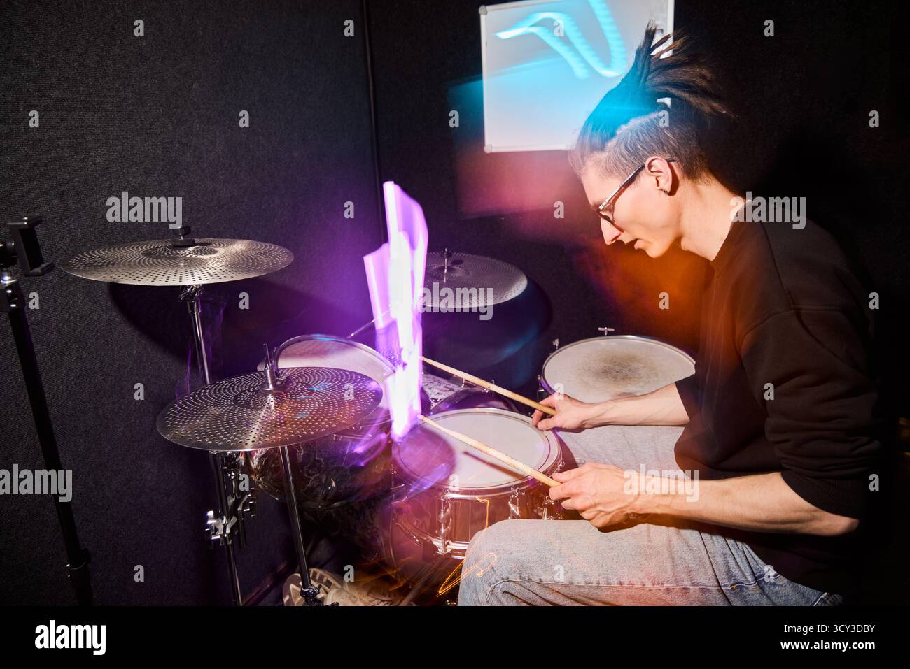 Drummer performing in a studio with vibrant lighting effects Stock Photo
