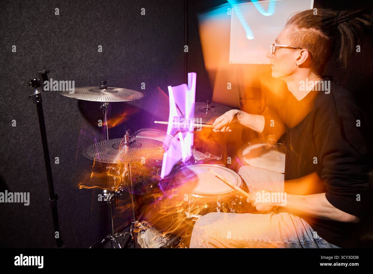 Drummer performing in a vibrant practice studio at night Stock Photo
