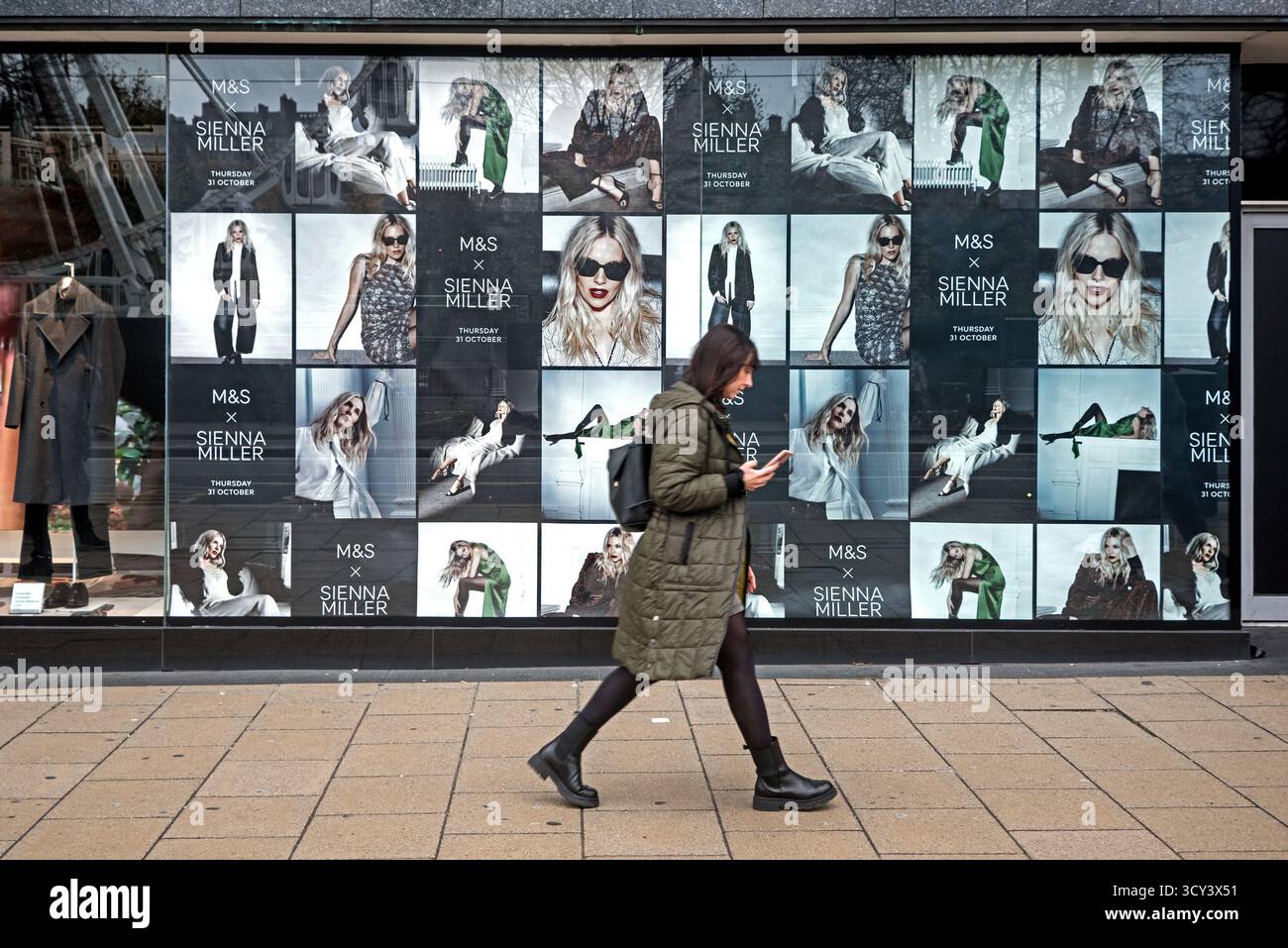Woman walking past Sienna Miller photos displayed in the window of ...