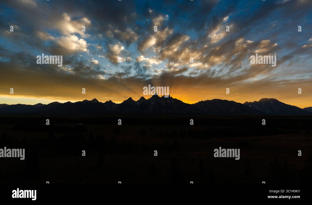 Sunset rays of colorful light sweep over a panoramic mountain scene ...