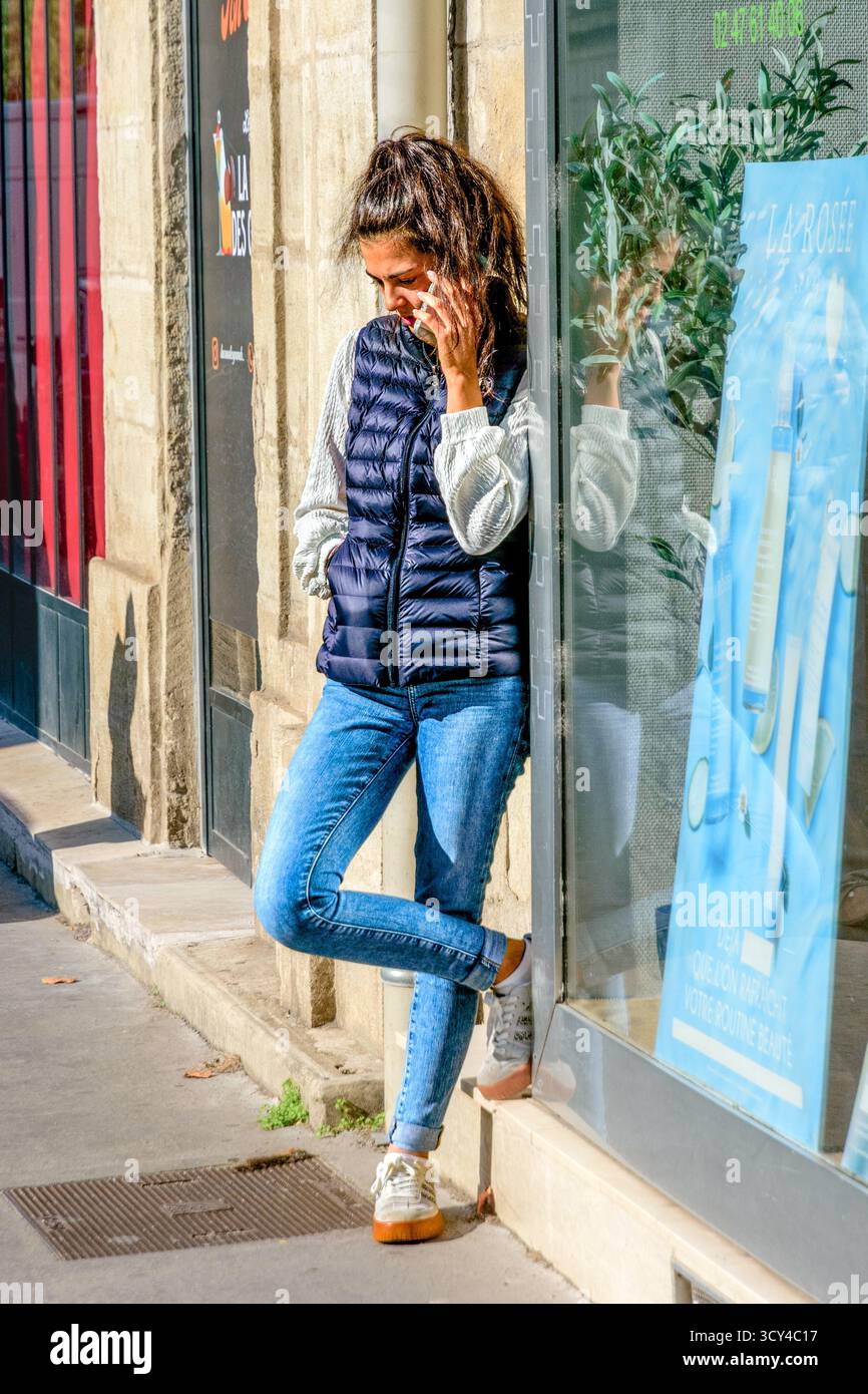 Young woman on mobile phone leaning on shop frontage - Tours, Indre-et-Loire (37), France. Stock Photo