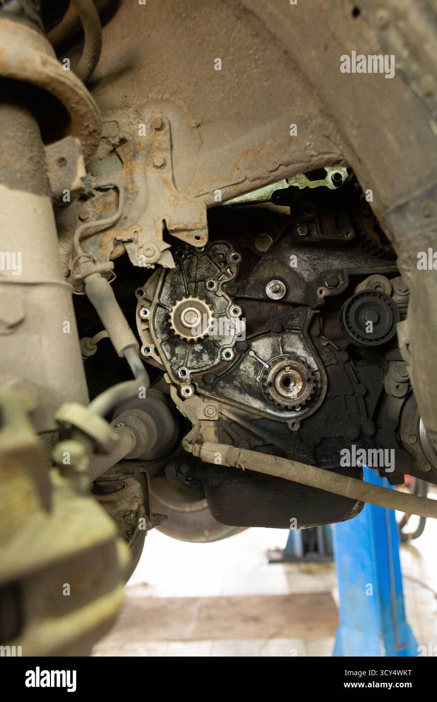 A close-up shot of a dirty and oily car engine, showing the timing belt and pulleys, as seen from underneath a vehicle during maintenance or repair. Stock Photo
