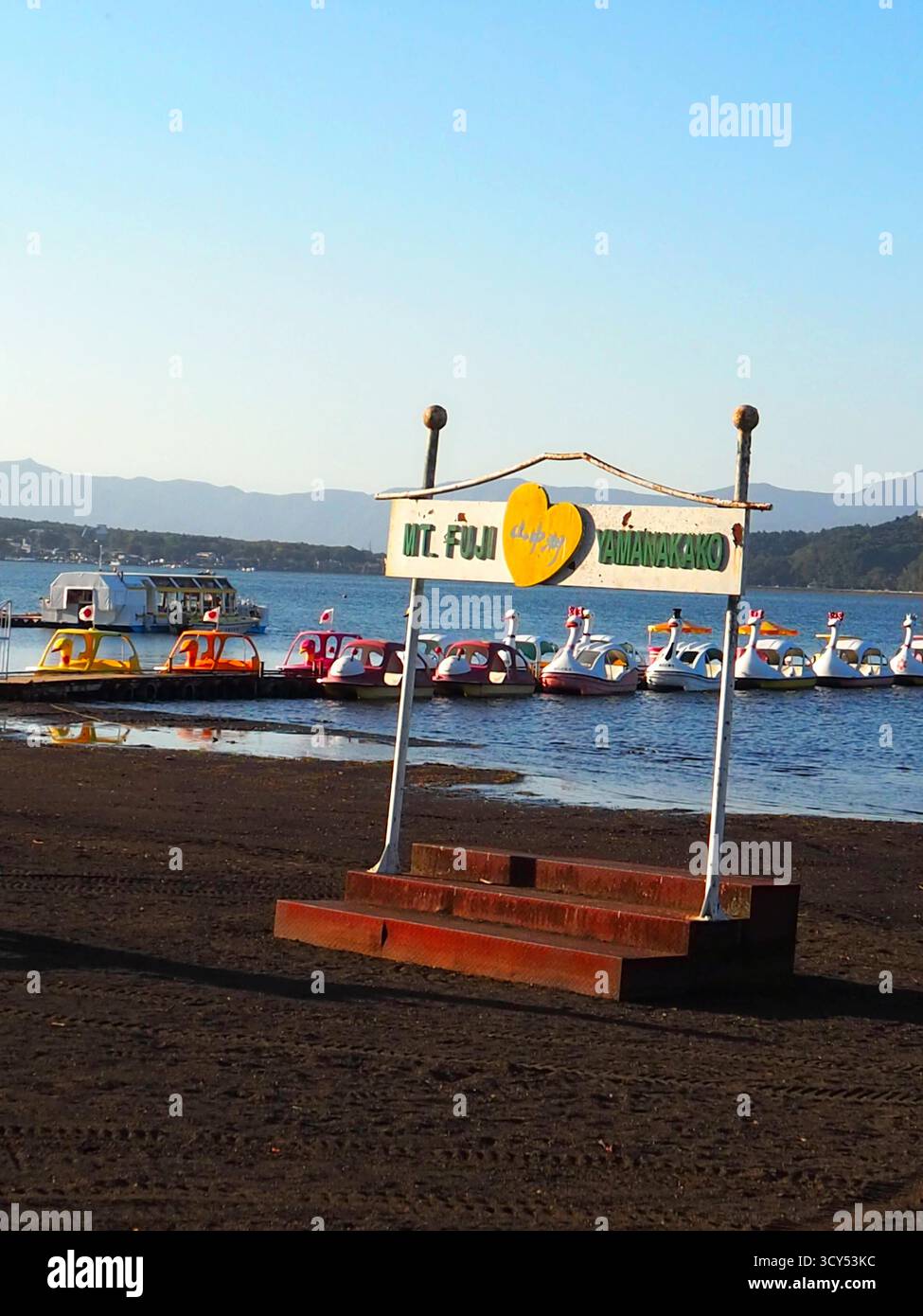 Swan boats lined up on Lake Yamanaka under clear autumn sky with Mt. Fuji sign at lakeside photo spot in Japan Stock Photo