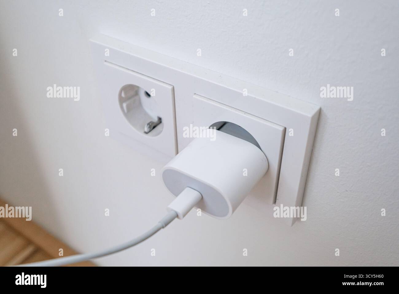 USB charging cord inserted into a wall power socket Stock Photo