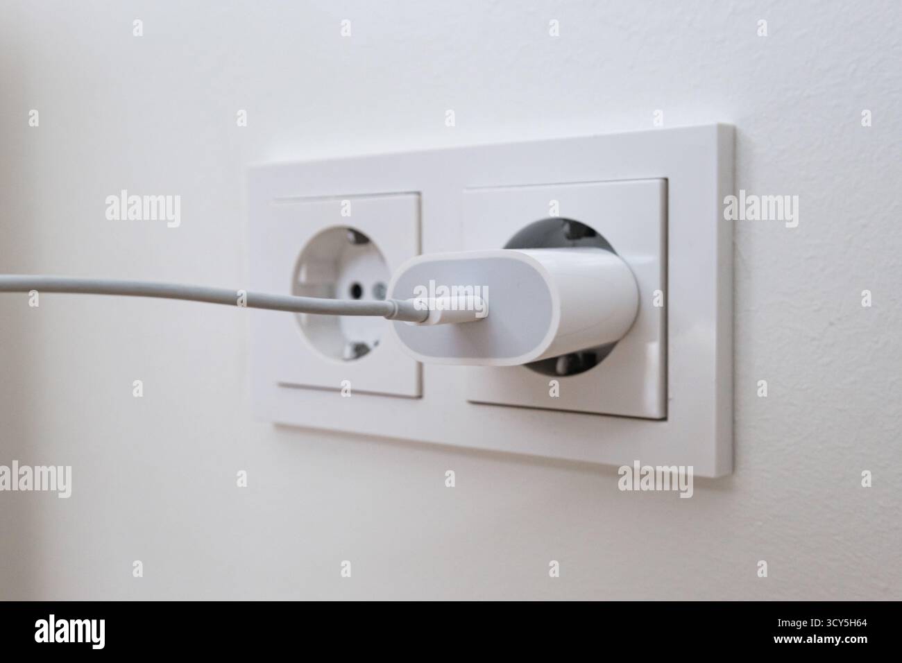 USB charging cord inserted into a wall power socket Stock Photo