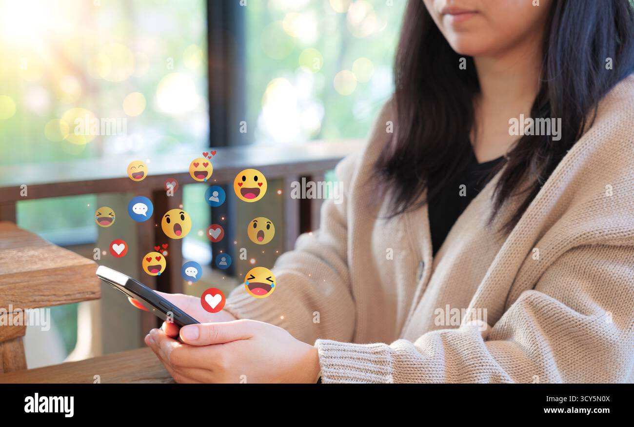 Engaging with social media on the phone. Woman use a smartphone, with social media reactions and emojis floating around, representing online interacti Stock Photo