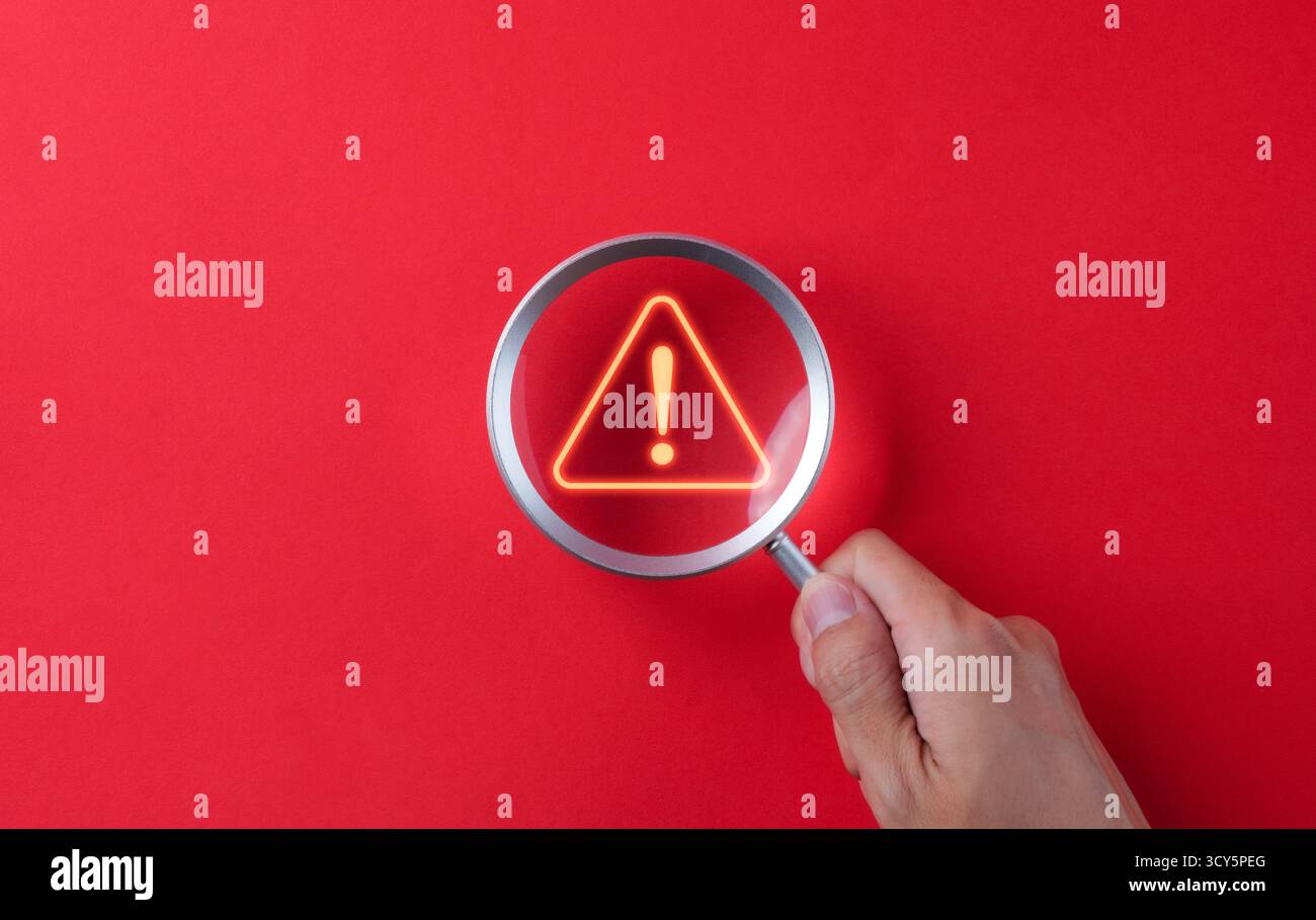 Warning alert system concept. A hand holds a magnifying glass over a ...
