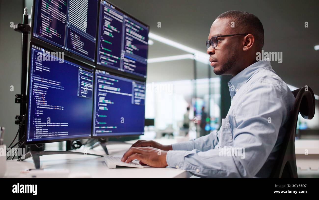 African American Man Coding On Multiple Computer Screens In Office. Stock Photo