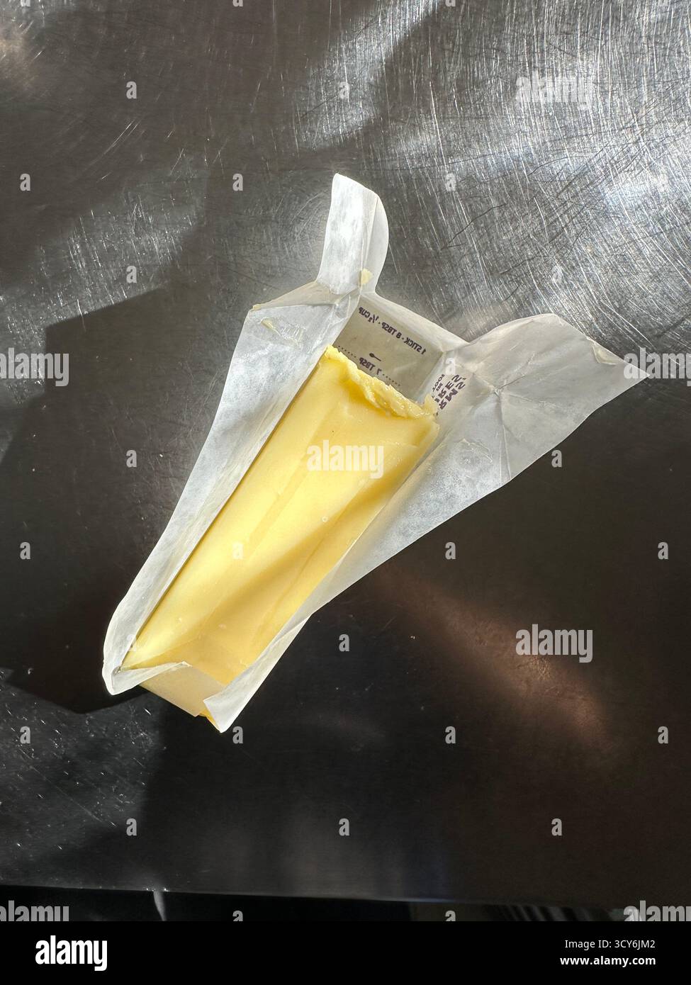 butter stick partly unwrapped top view on kitchen table in morning sun light - Smartphone Captured Stock Image