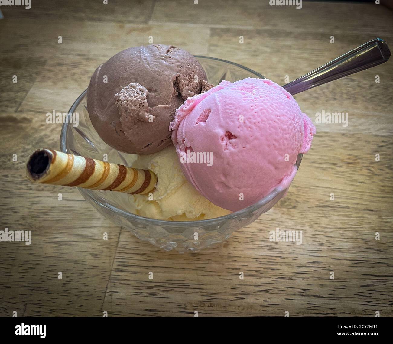 Three scoops of ice cream — strawberry, chocolate, and vanilla — served in a glass dessert bowl with a wafer stick. Refreshing summer dessert - Smartphone Captured Stock Image