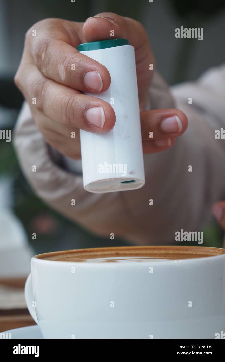 Hand adding sweetener sugar substitute in a coffee  Stock Photo