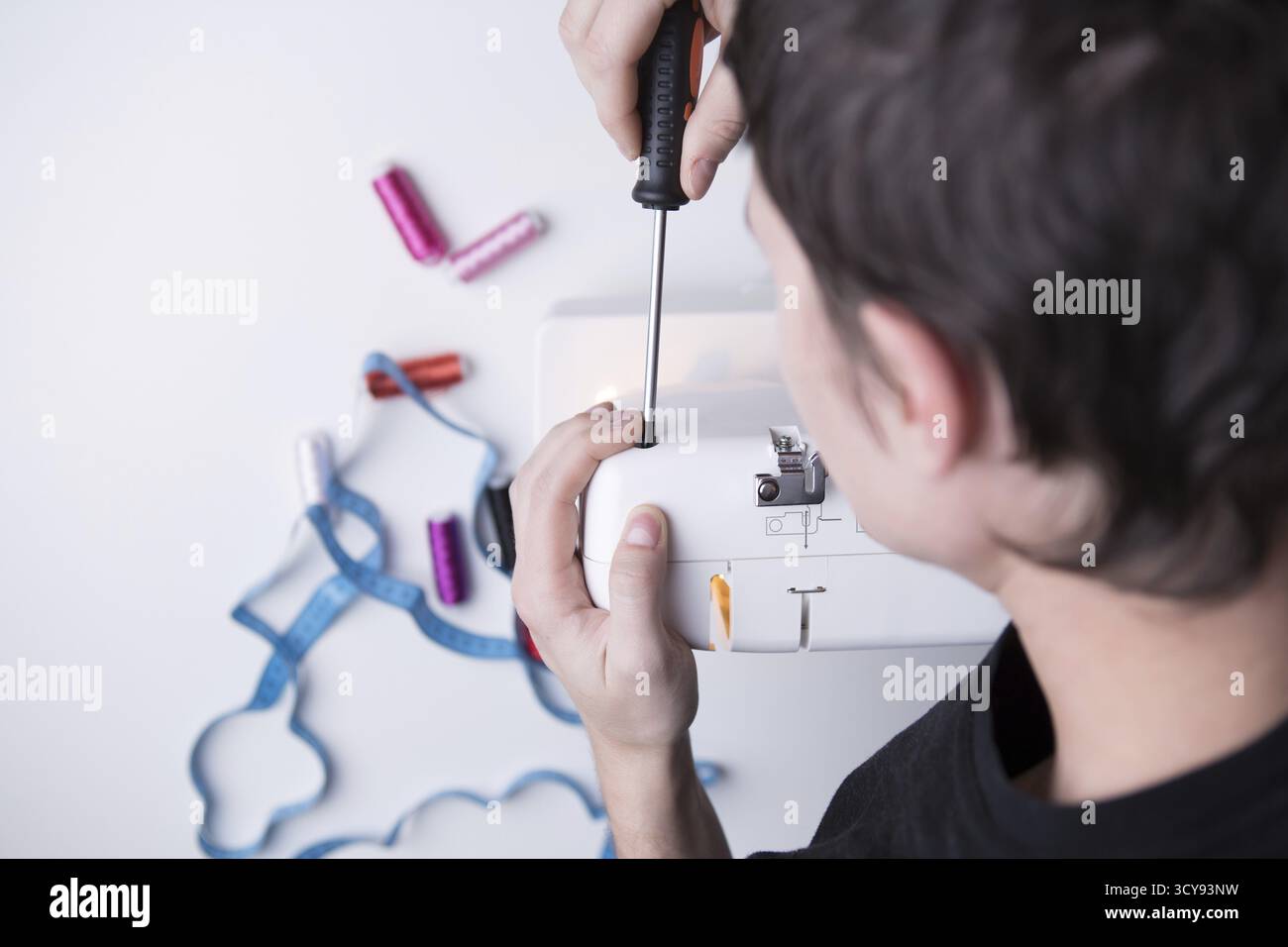 Man with screwdriver repairing sewing machine on empty gray background Stock Photo