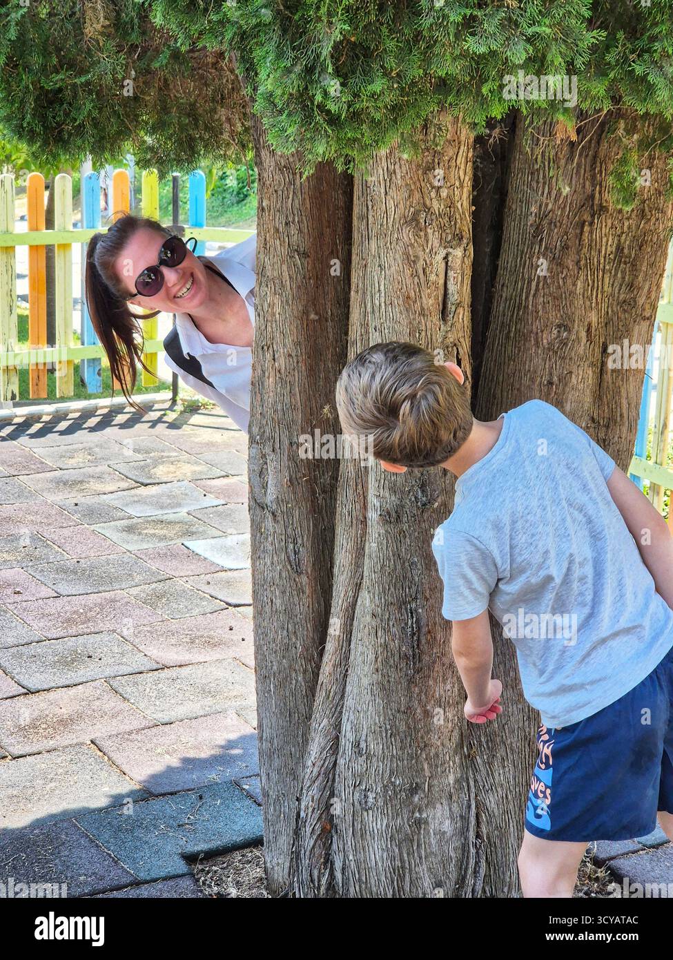 mother and son spending time together. playing outside. summer vacation. hide and seek behind the tree - Smartphone Captured Stock Image