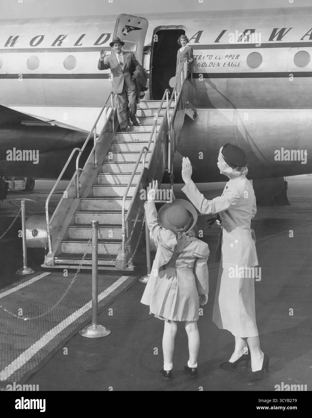 Businessman standing on the steps of an airliner waving goodbye to his wife and child Stock Photo