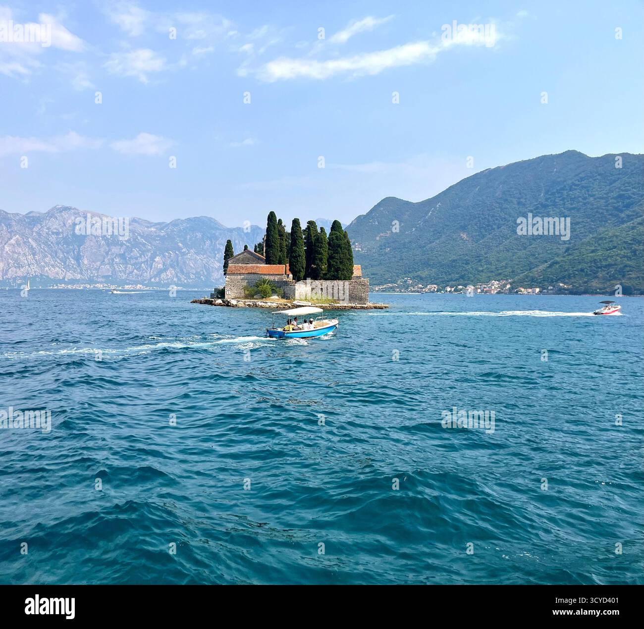 A small island with a historic stone building and tall cypress trees surrounded by clear blue water and mountains in the background. - Smartphone Captured Stock Image A small island with a historic stone building and tall cypress trees surrounded by clear blue water and mountains in the background. - Smartphone Captured Stock Image