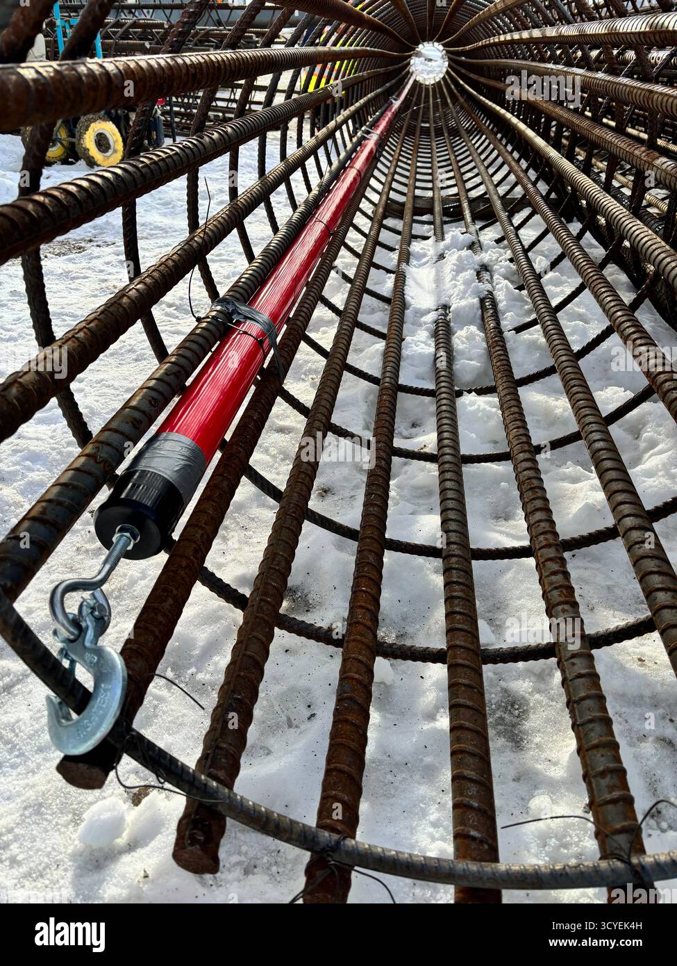 Close-up inside view of a cylindrical rebar reinforcement cage with red conduit and lifting hook, used for concrete foundation construction in winter. - Smartphone Captured Stock Image