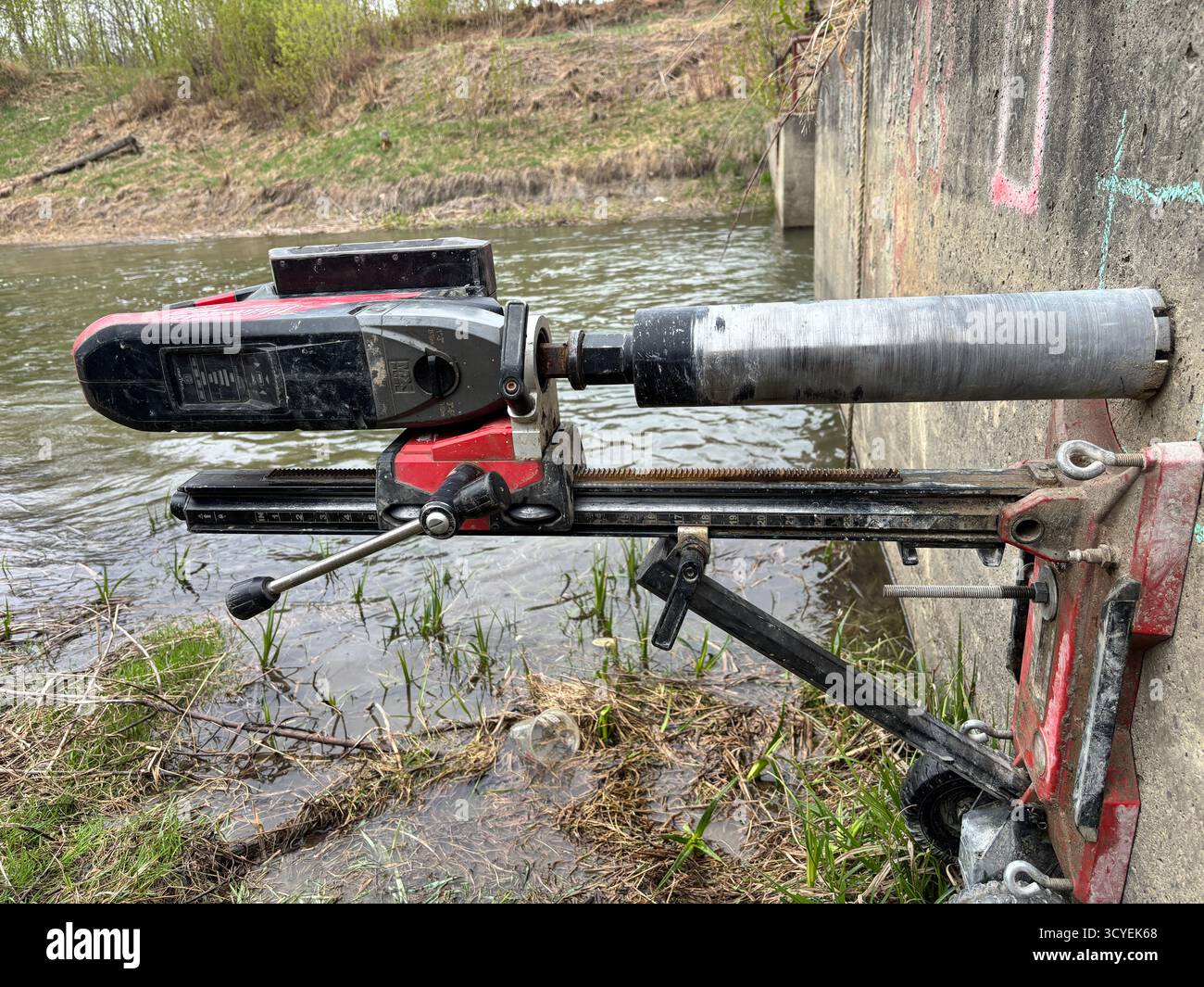 Milwaukee core drill mounted on a concrete wall near a river during construction. - Smartphone Captured Stock Image