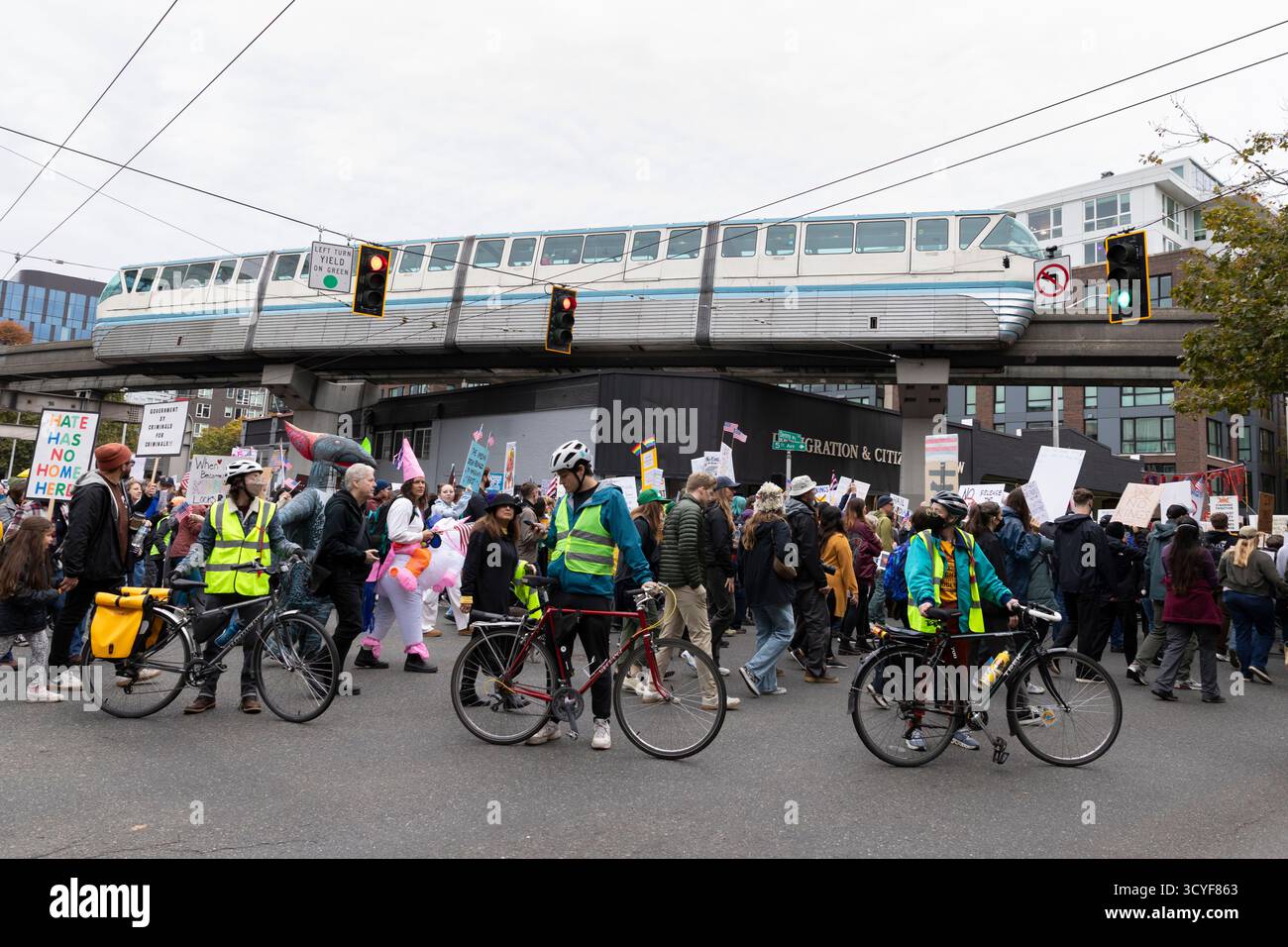 Seattle, Washington, USA. 18th October 2025. Volunteers on bicycles block the streets for protesters as the monorail passes during the “No Kings” protest and march. An estimated 90,000 people attended the mass protest as part of a national day of peaceful action organized by the No Kings coalition in response to perceived authoritarian actions and corruption of the Trump administration. Credit: Paul Christian Gordon/Alamy Live News Stock Photo