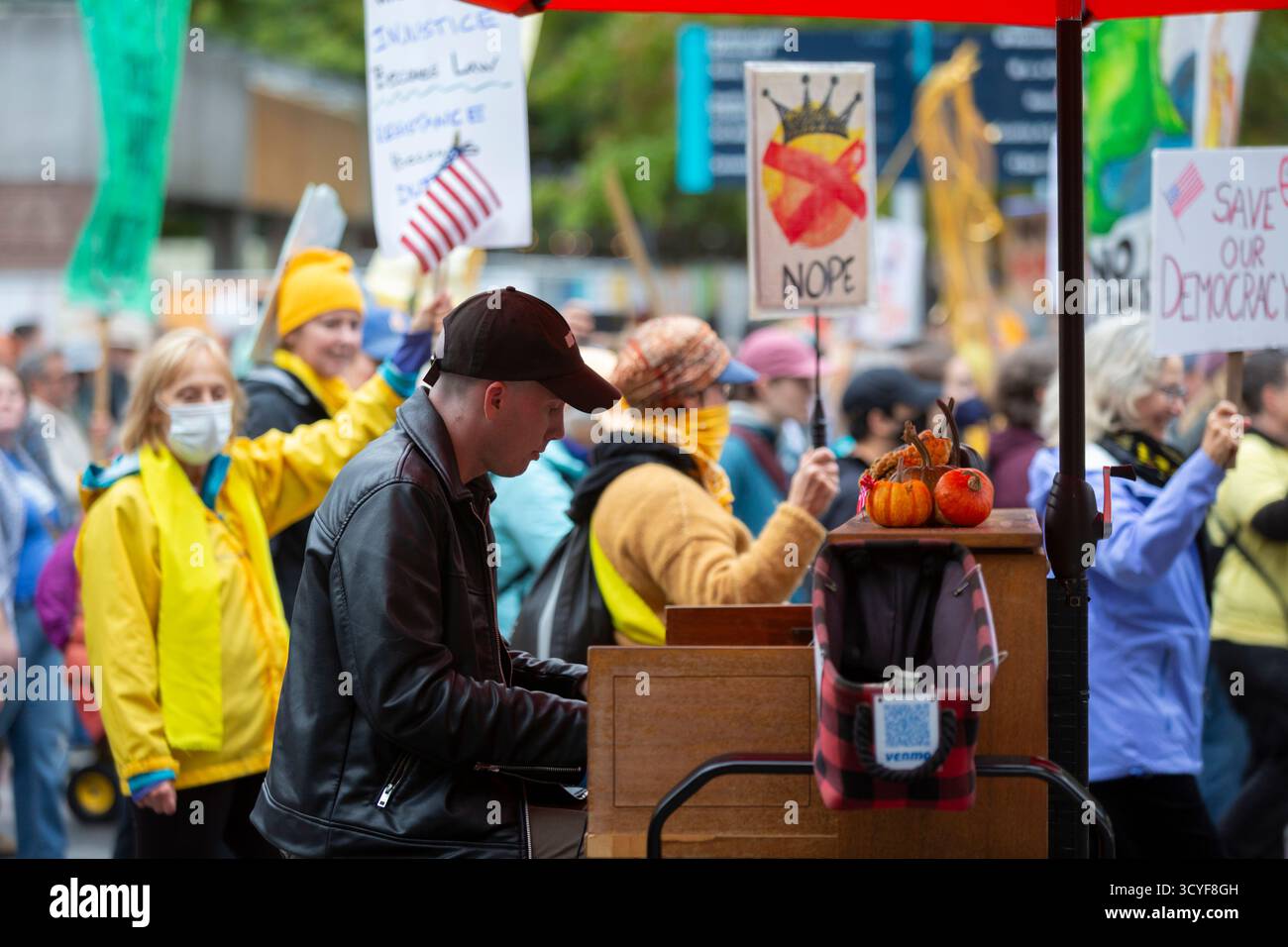 Seattle, Washington, USA. 18th October 2025. A busker plays the piano as protesters pass by during the “No Kings” protest and march. An estimated 90,000 people attended the mass protest as part of a national day of peaceful action organized by the No Kings coalition in response to perceived authoritarian actions and corruption of the Trump administration. Credit: Paul Christian Gordon/Alamy Live News Stock Photo