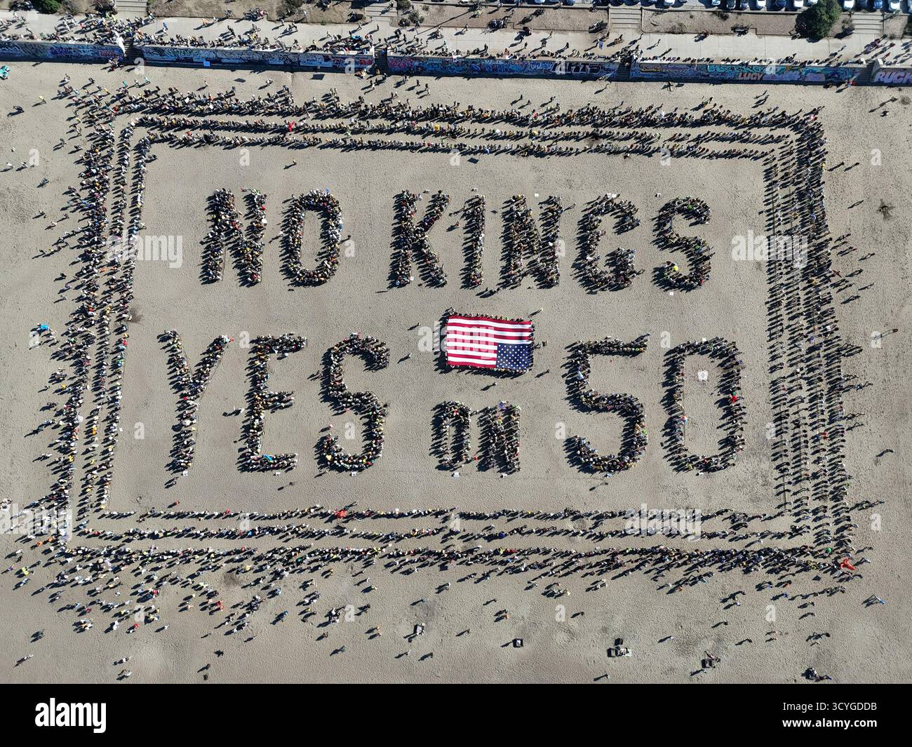 San Francisco, United States - 18 October 2025: Aerial view of a massive crowd forming 'NO KINGS YES ON 50' on the sandy expanse, punctuated by a vibrant American flag. Stock Photo