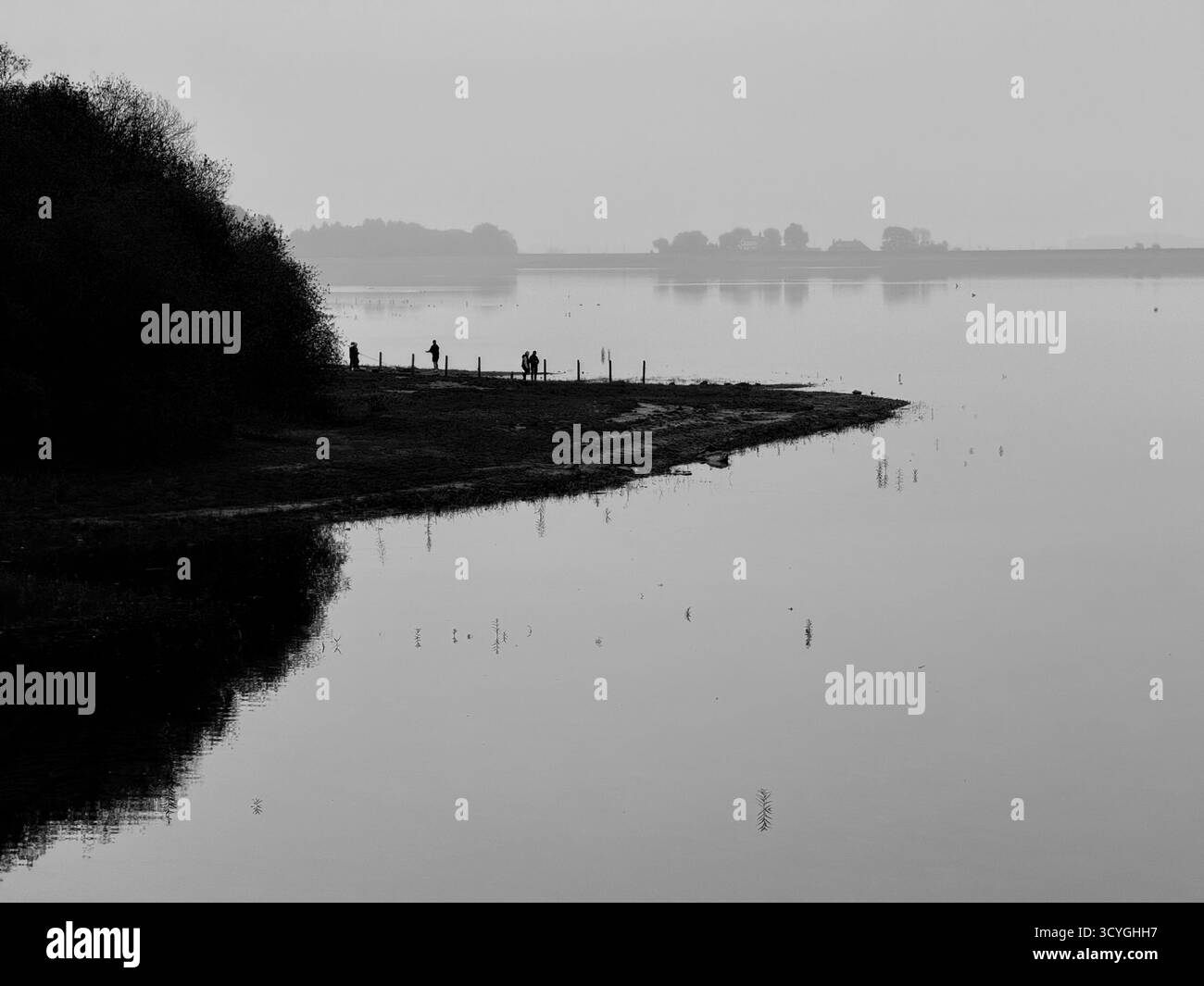 People in silhouette on beach on a misty day at Rivington lower reservoir near Chorley in Lancashire - Smartphone Captured Stock Image