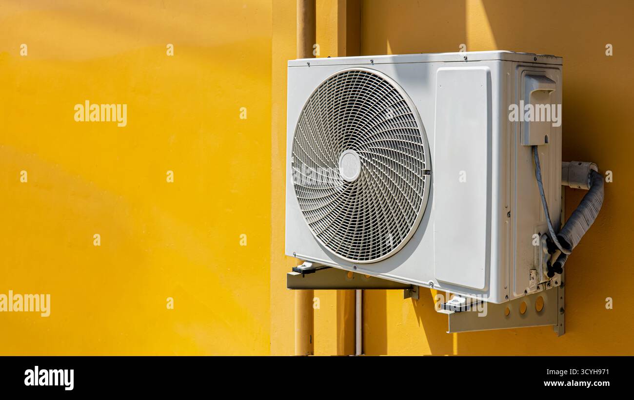 Outdoor air conditioner compressor unit on yellow wall with sunlight ...