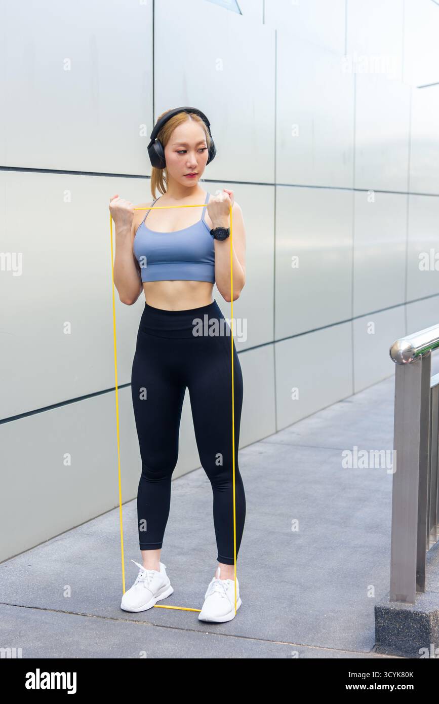Fit woman performs sport exercise workout outdoor, using resistance band for arm stretch, developing Stock Photo