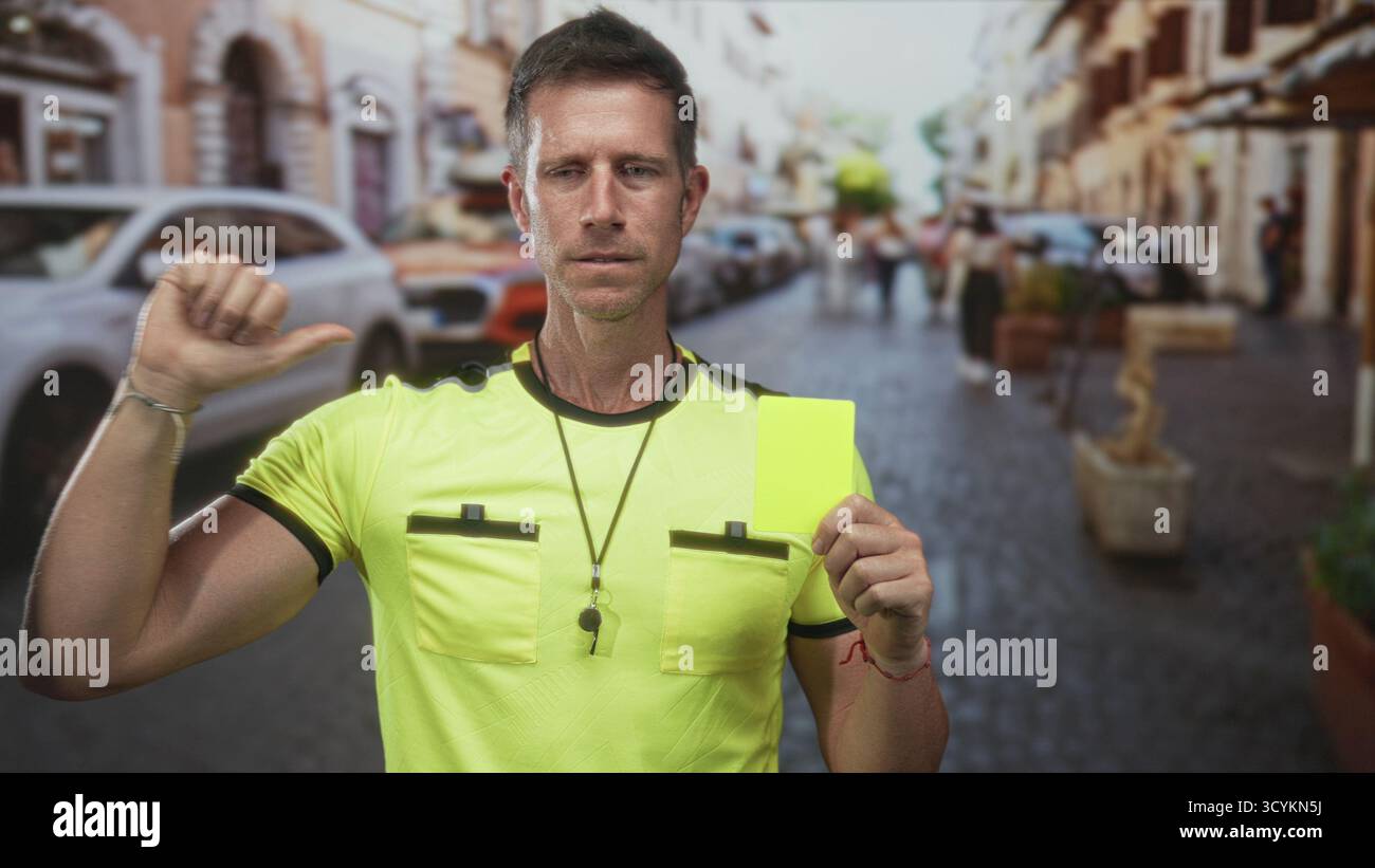 Man referee holding yellow card and whistle on street, thumb pointing ...