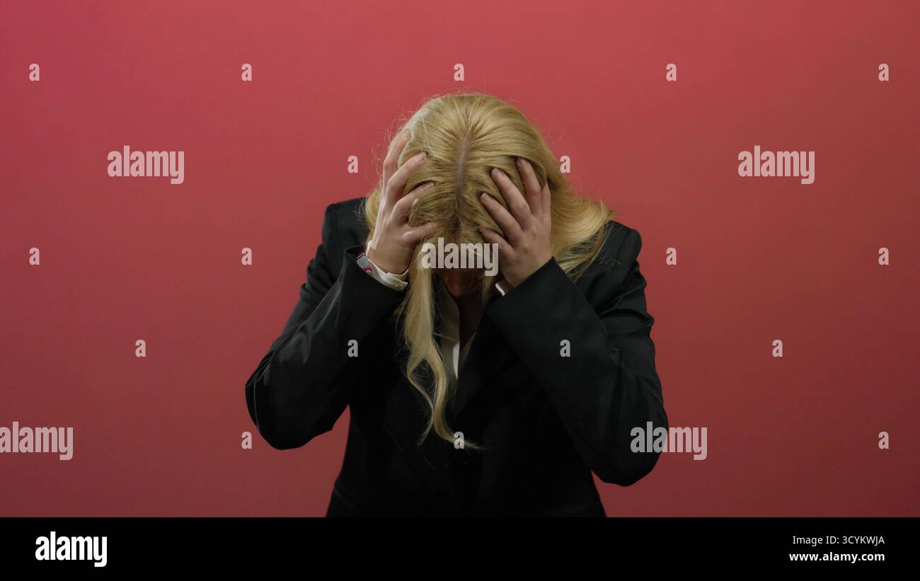 Woman with blonde hair looks distressed in front of a vibrant red ...