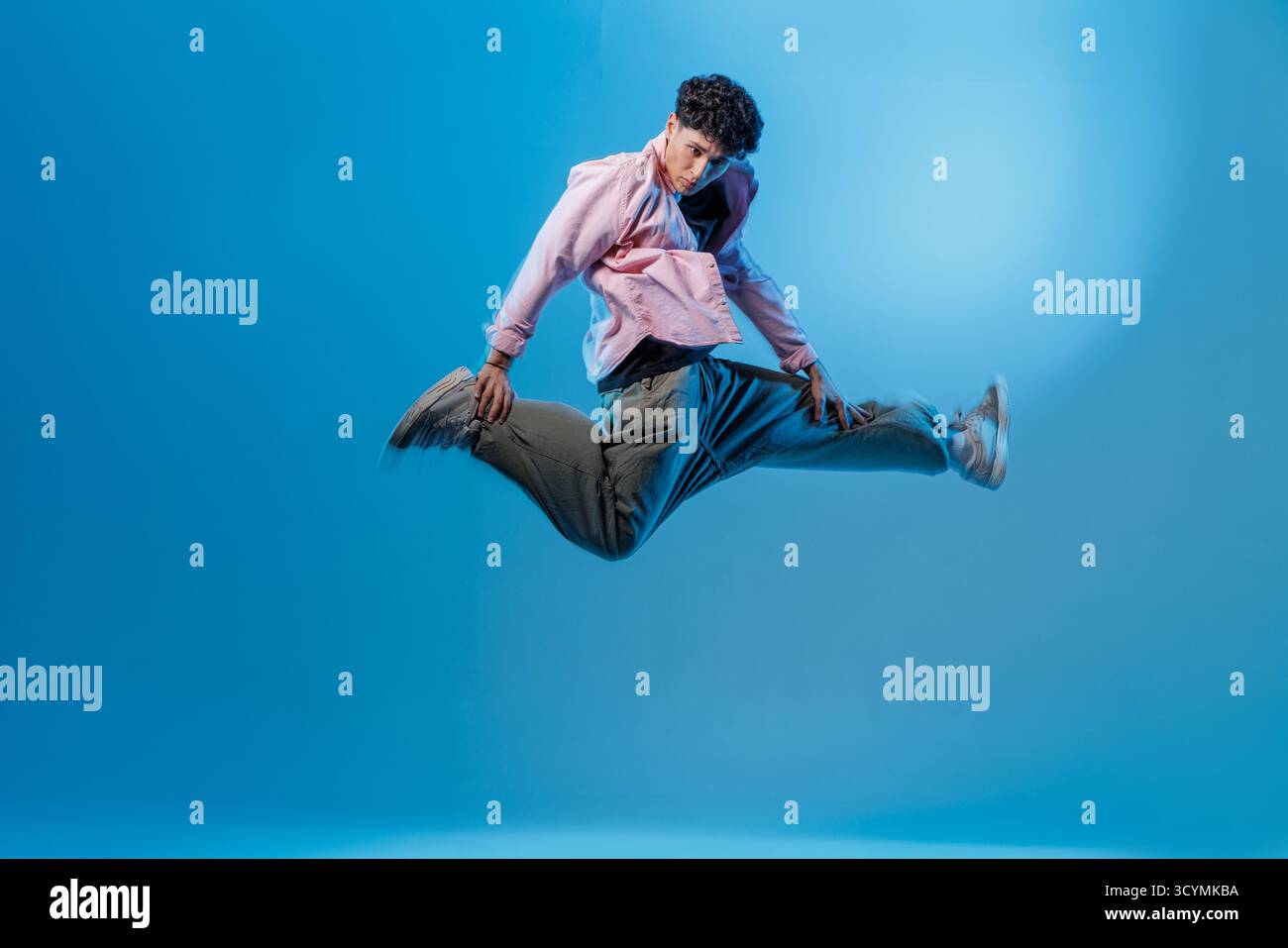 Breakdancer leaps midair in blue neon studio. Dynamic hiphop image for music events, ads, posters and social media with room for text. Stock Photo