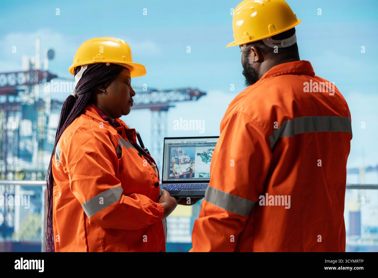 Drilling rig technicians brainstorming, using laptop software dashboard for anomaly detection during operation. Teamworking offshore platform colleagues use notebook to control systems remotely Stock Photo
