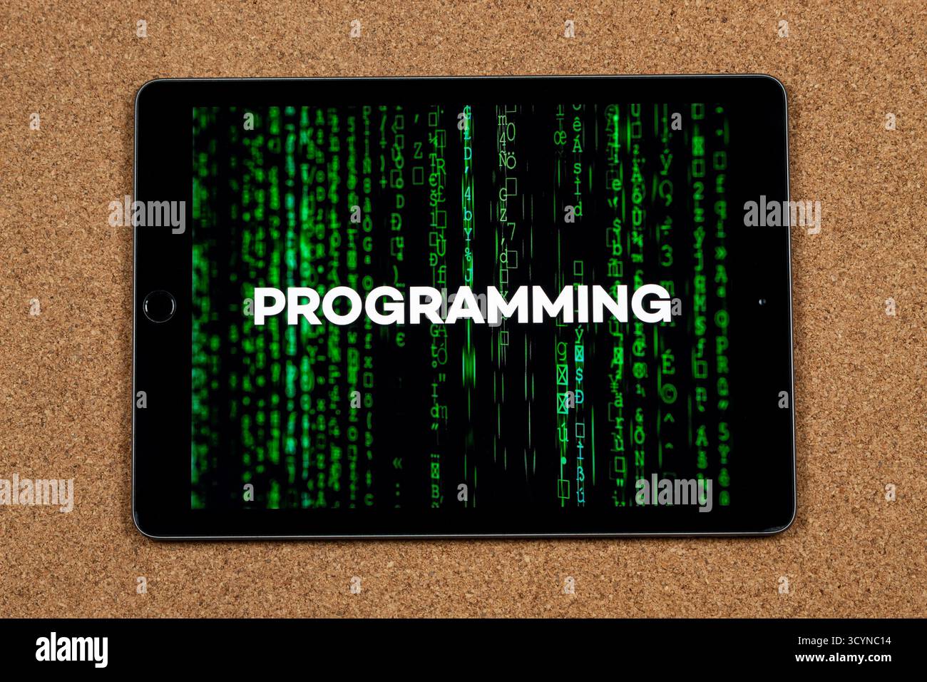 Close up to a tablet with the word programming over a green matrix code concept with a cork background Stock Photo