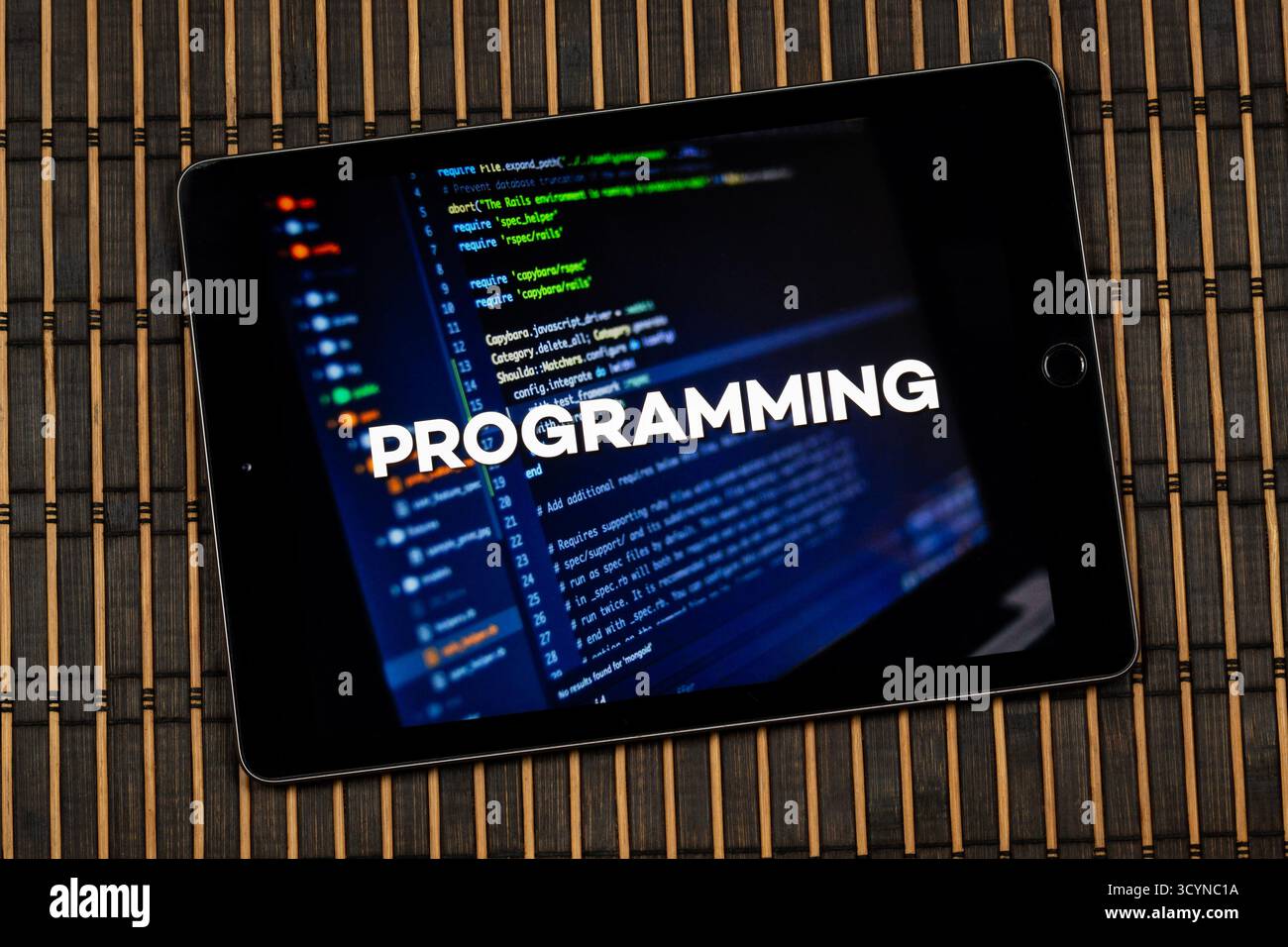 Close up to a tablet with the word programming over a writing code concept and a wooden background Stock Photo