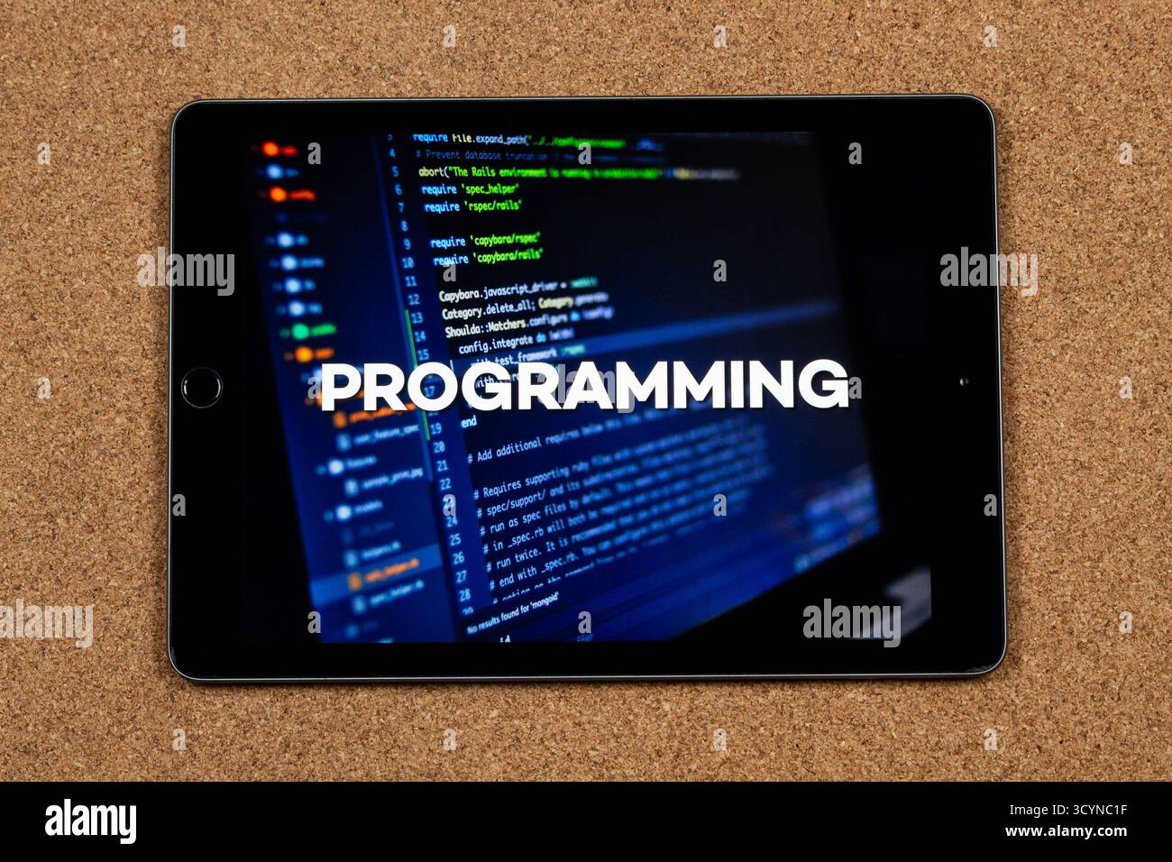 Close up to a tablet with the word programming over a writing code concept and a cork background Stock Photo