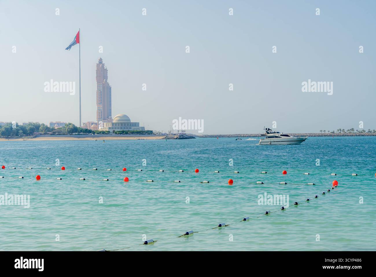 UAE Flag and Landmark Tower on Corniche waterfront, Abu Dhabi, UAE, with luxury yacht and turquoise waters during daytime. Stock Photo