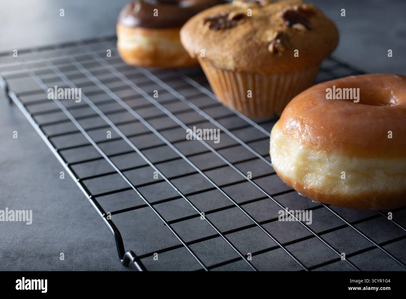 A view of donuts and muffins on a wire cooling rack, on the right side of the frame. Stock Photo